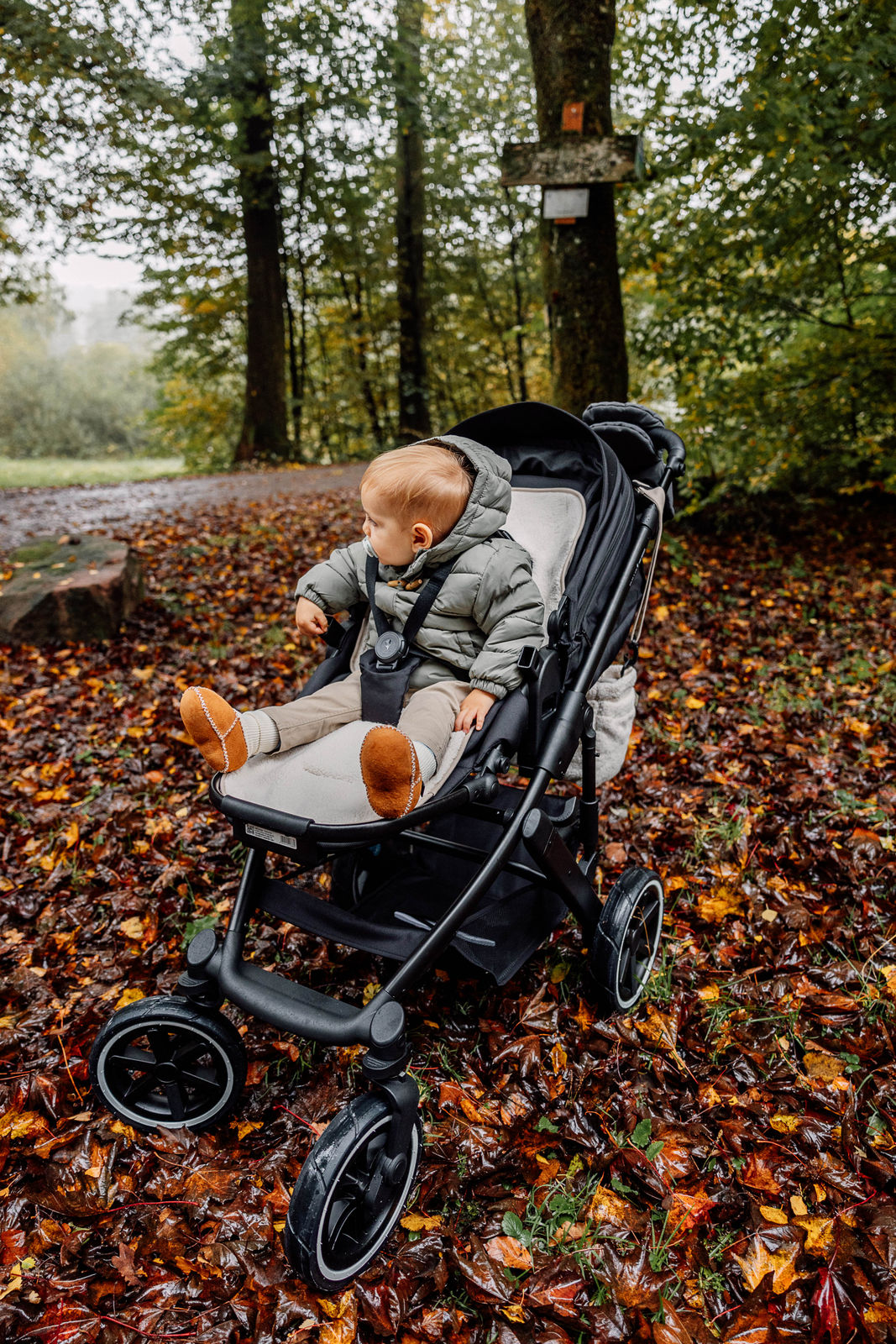Kind sitzt im Kinderwagen auf der Kinderwagenauflage in Farbe ivory - Winterseite.
