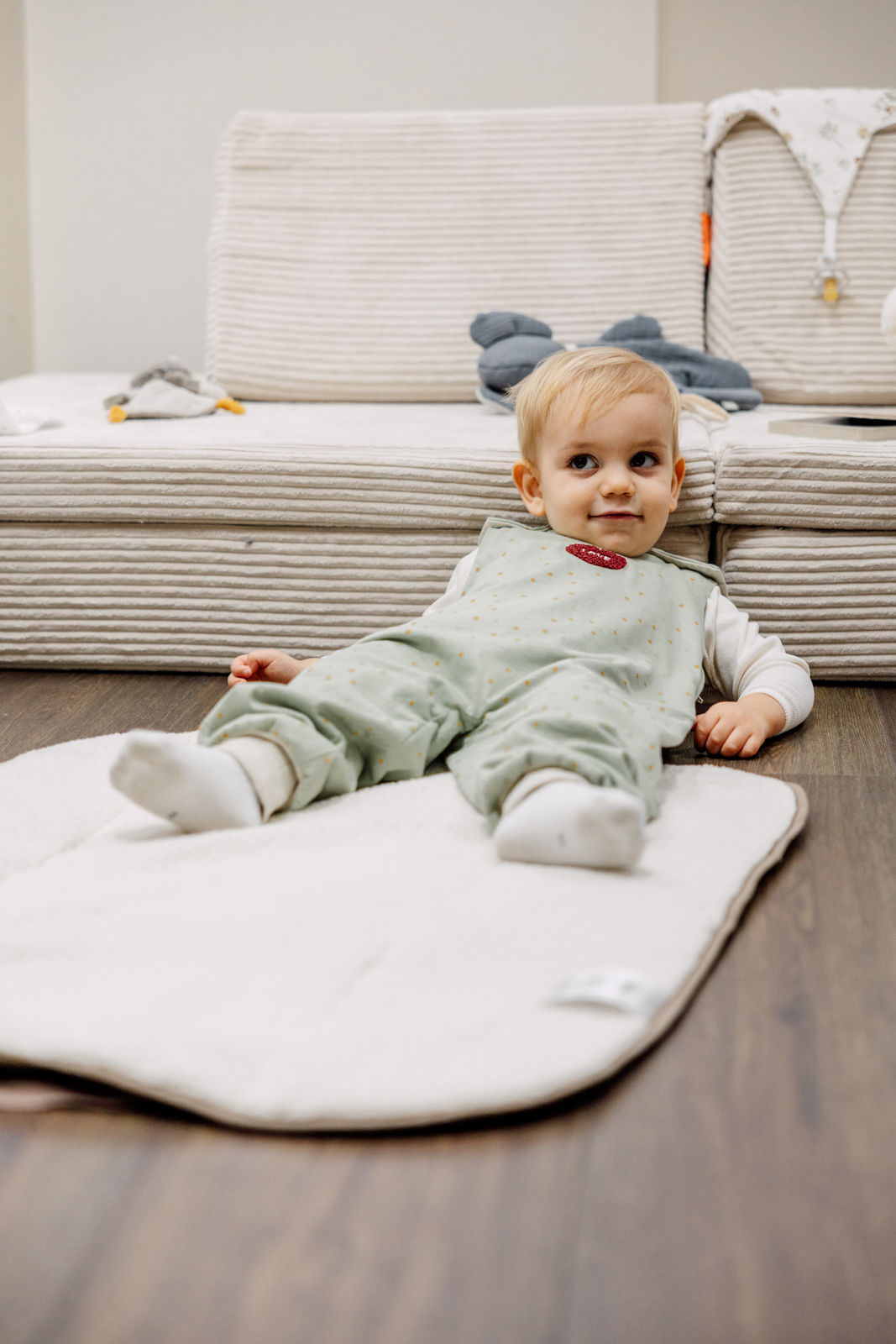 Aktives Kind sitzt entspannt auf dem Boden im Odenwälder Sommer Jersey-Hopsi Babyschlafsack, mintgrün mit Punktmuster, atmungsaktiv und leicht, ideal für warme Sommernächte, bequem und flexibel für Kinder, die schon flitzen und sich viel bewegen