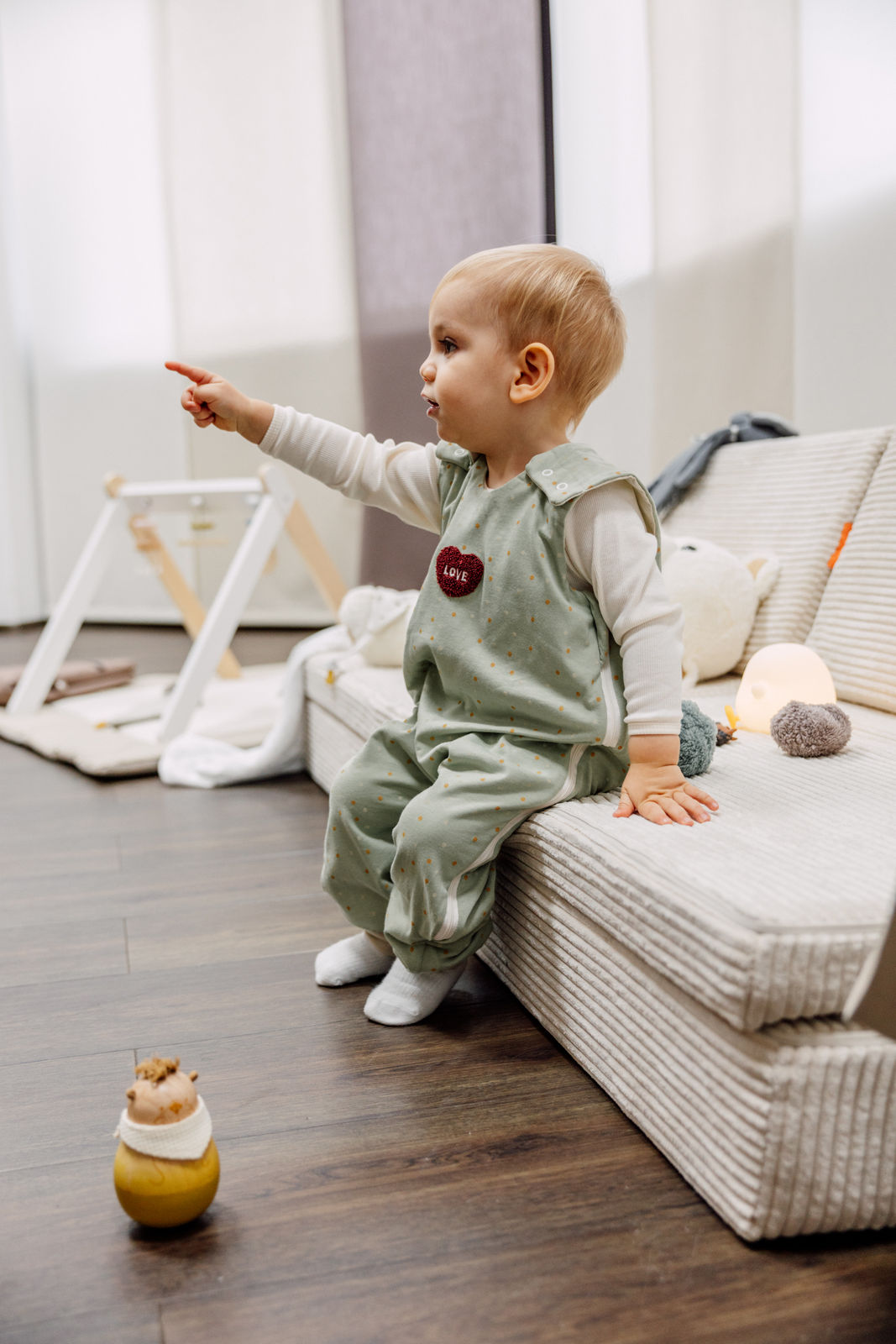 Aktives Kind sitzt entspannt auf dem Sofa im Odenwälder Sommer Jersey-Hopsi Babyschlafsack, mintgrün mit Punktmuster, atmungsaktiv und leicht, ideal für warme Sommernächte, bequem und flexibel für Kinder, die schon flitzen und sich viel bewegen