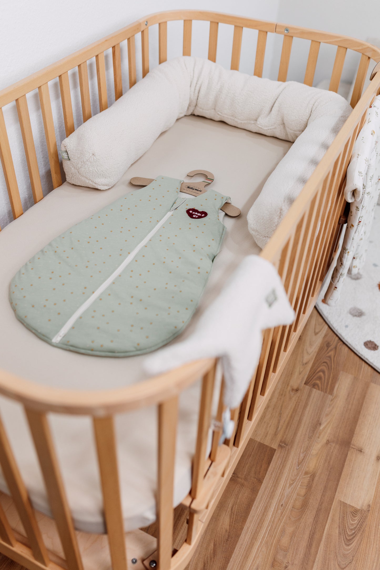 Mintgrüner Ganzjahres-Jersey-Schlafsack mit Punktmuster liegt in einem Babybett, ärmelloser Schlafsack mit Reißverschluss und Herz-Patch „HUG“.