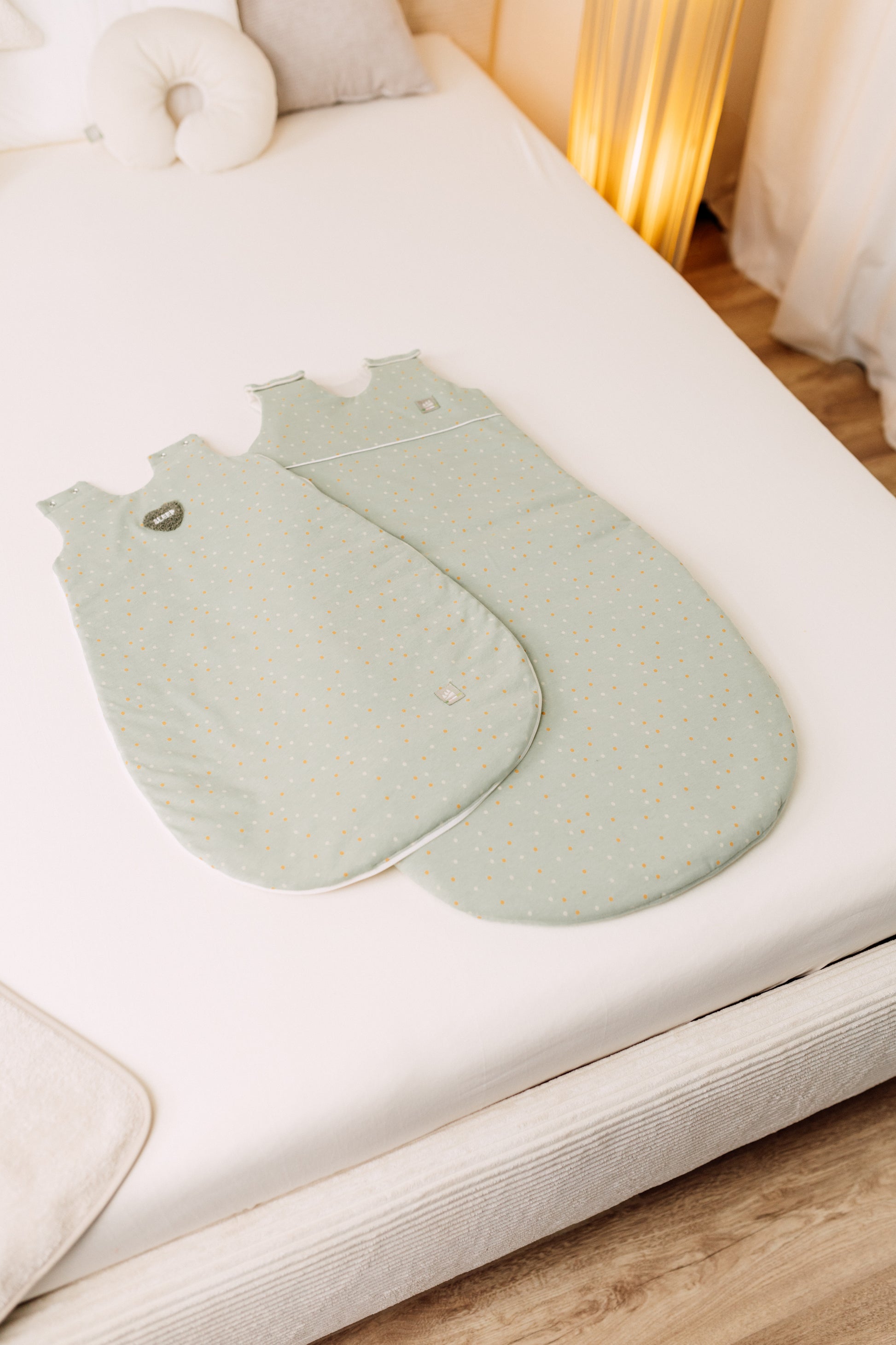 Übersicht des Ganzjahres mitwachsenden Jersey-Schlafsacks in der Designvariante Dotty, präsentiert auf einem Bett, zeigt die Variante mit kurzem und langen Vorderteil nebeneinander.