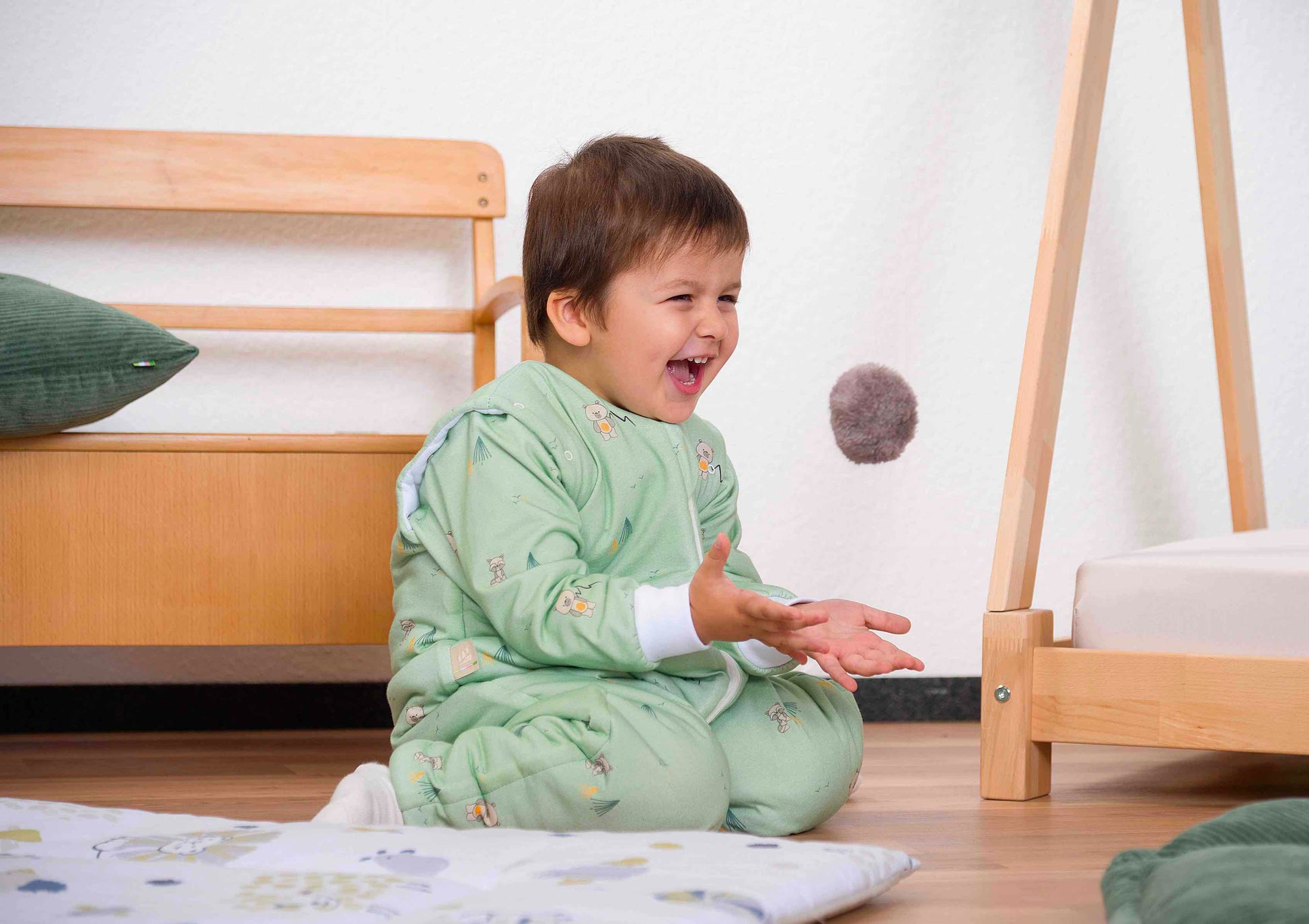 Beispielkind trägt den Hopsi wattierten Babyschlafsack in der Designvariante Twofriends Greenery, gezeigt in einer Alltagssituation zur Demonstration aller Hopsi wattiert Varianten.